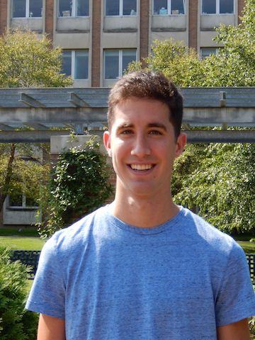 Adam Kawash smiling in a blue shirt with green trees.